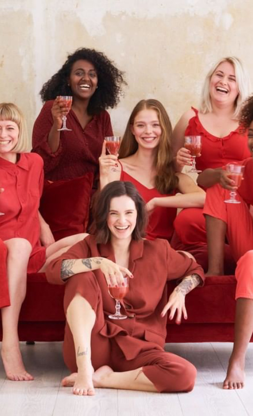 group of women laughing on sofa with drinks in hand portrait format